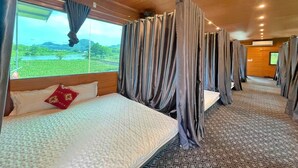 A train car with a bed, curtains, and a window with a view of greenery. - Hideaway Village Homestay (Hoa Lu)