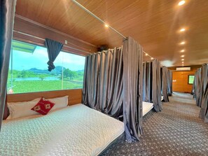 Un vagón de tren con cama, cortinas y una ventana que da a vistas de vegetación.
