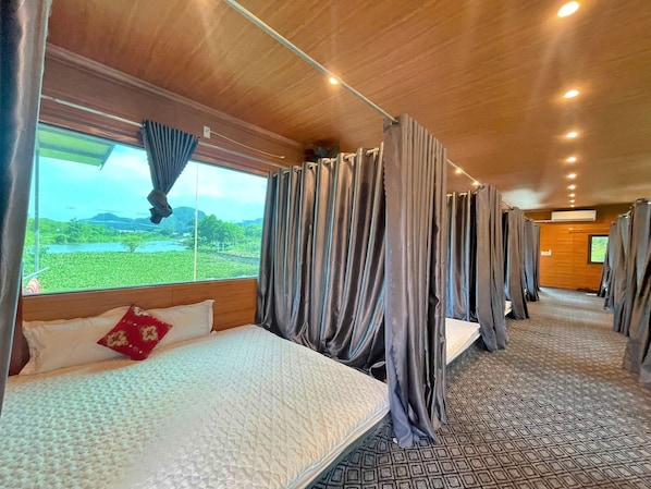 A train car with a bed, curtains, and a window with a view of greenery.