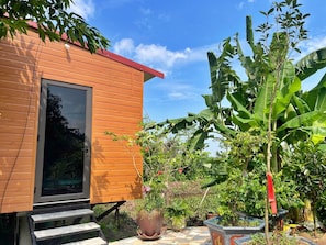 A wooden building with a glass door, surrounded by lush greenery and a tiled patio.