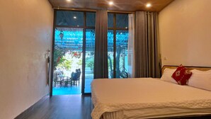 A bedroom with a bed, a view of an outdoor seating area, and a window with curtains. - Hideaway Village Homestay (Hoa Lu)