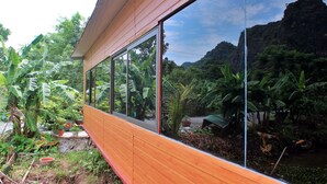 A wooden building with large windows overlooking a lush garden and a river. - Hideaway Village Homestay (Hoa Lu)