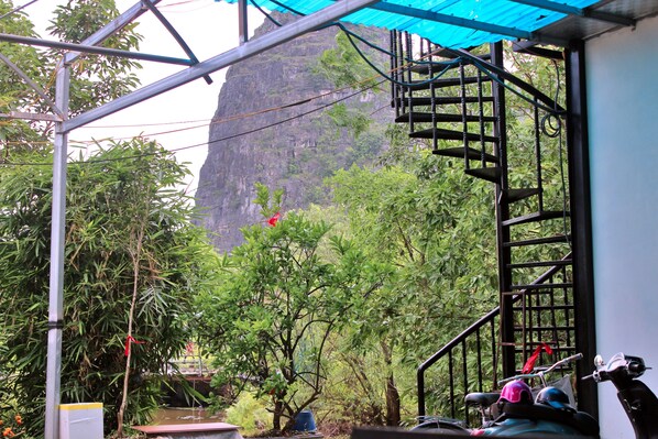 A room with a staircase, a view of a mountain, and greenery outside.