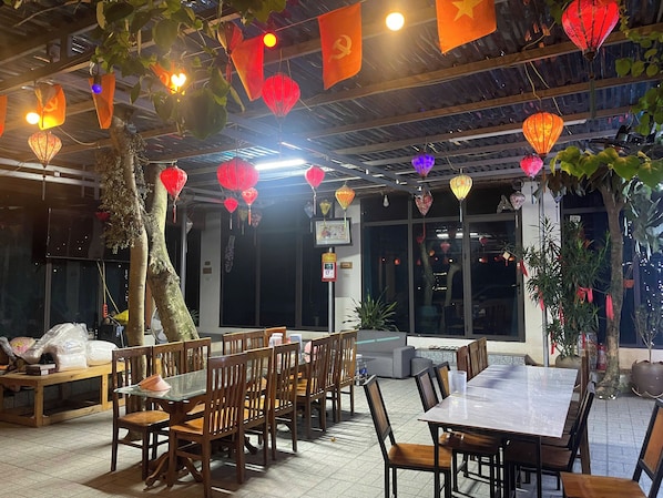 Un restaurante con mesas y sillas de madera, faroles rojos y plantas en macetas.