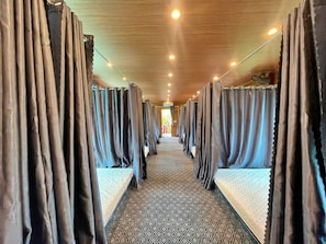 Un pasillo de hotel con hileras de habitaciones con cortinas, alfombra estampada y techo de madera.