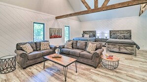 Ruime loft slaapkamer met een hoogslaper, twee leren sofa’s, een salontafel en een groot raam.