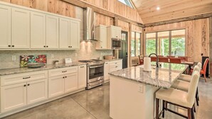 Een moderne keuken met witte kasten, roestvrijstalen apparatuur en een groot kookeiland met barstoelen.