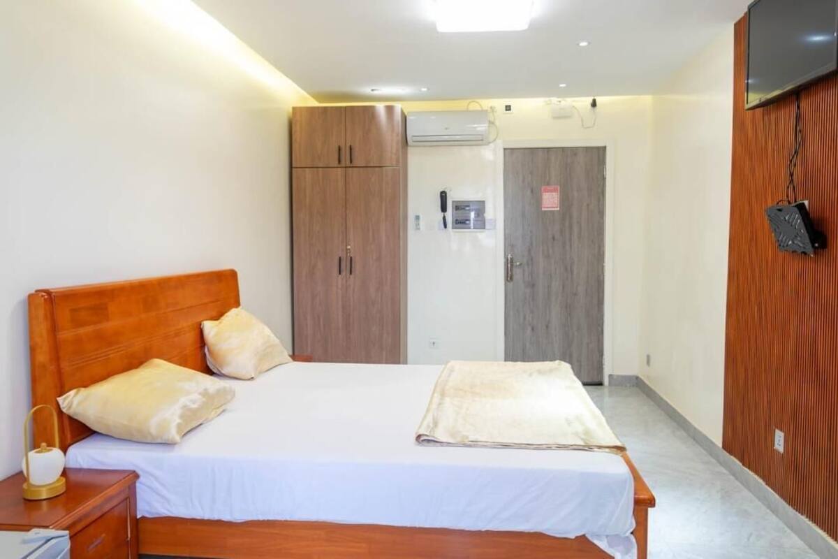 A hotel room with a wooden bed, a bedside table, a wardrobe, and a television mounted on the wall.