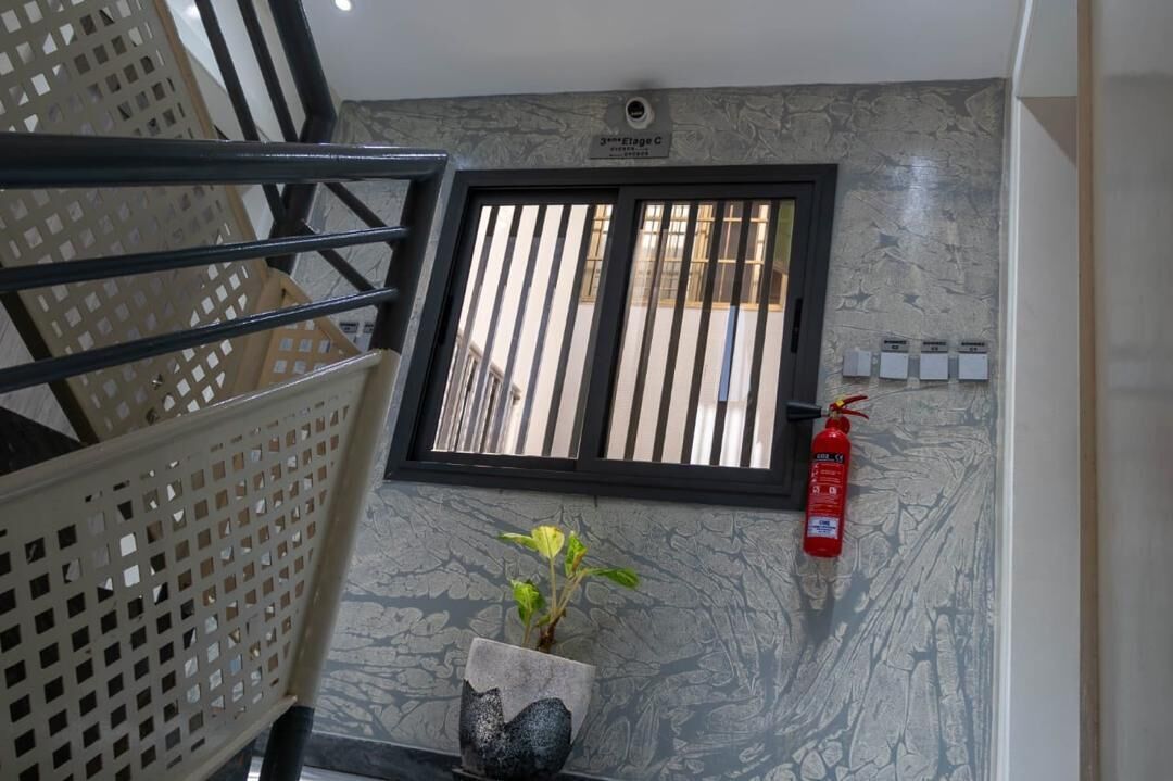 A staircase with a metal railing, a window with vertical bars, a fire extinguisher, and a potted plant.