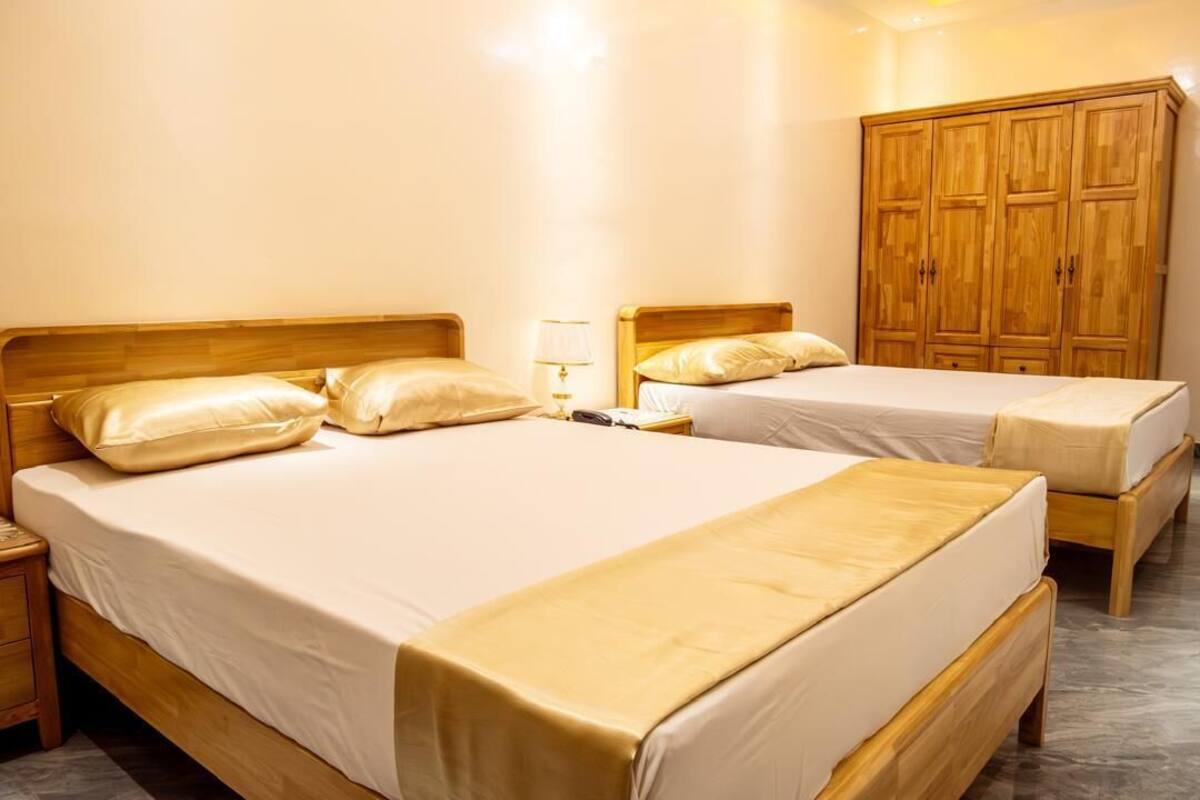 A hotel room with two single beds, wooden headboards, a nightstand with a lamp, and a wardrobe.
