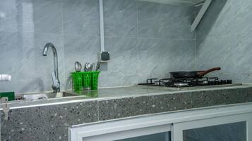 A kitchen with a sink, faucet, green basket, stove, and marble backsplash.