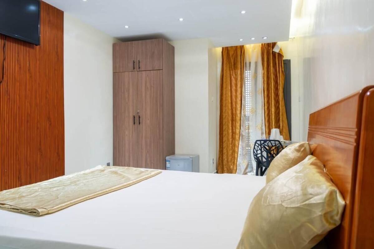 A hotel room with a bed, a television mounted on the wall, a wardrobe, and a desk with a chair.