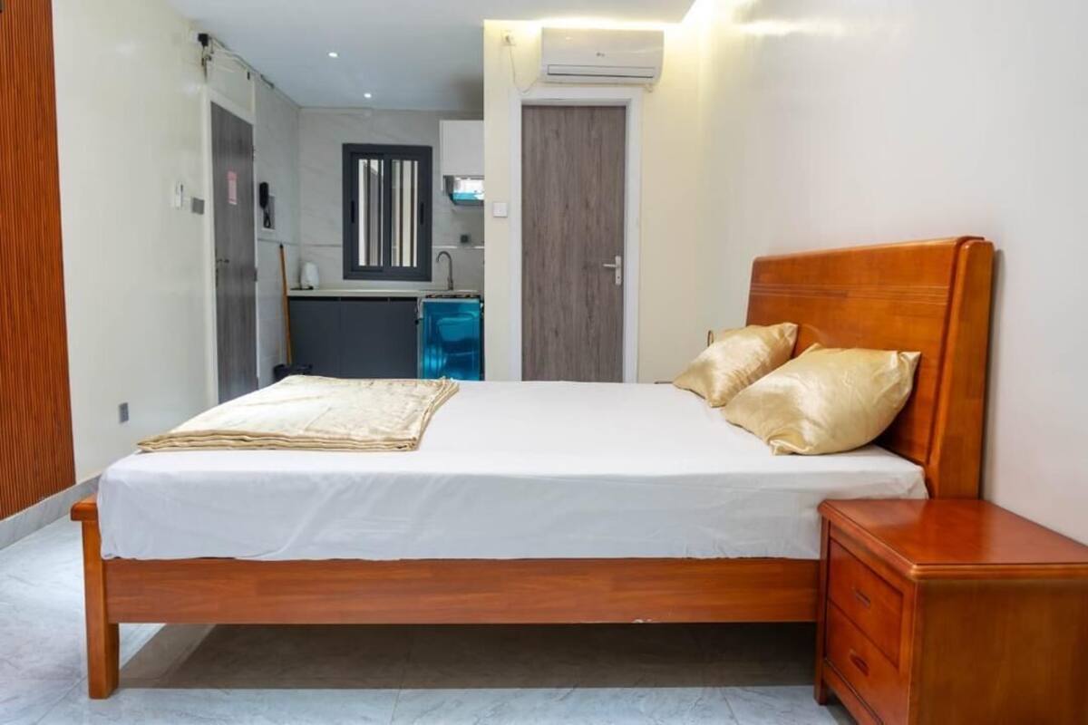 A bedroom with a wooden bed, a bedside table, and a view of a kitchen area.