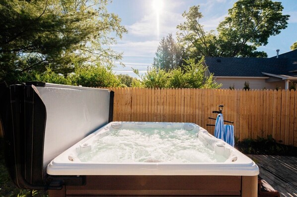 Een jacuzzi in een achtertuin met een houten omheining, bomen en een huis op de achtergrond.