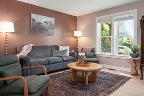 Ein Wohnzimmer mit Sofa, Sesseln, Couchtisch, Teppich, einem Gemälde und einem Fenster mit Aussicht.