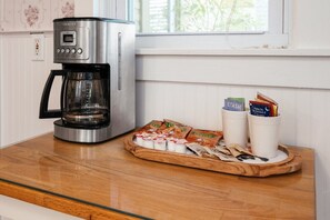 Eine Kaffeemaschine, eine Serviertablett mit Snacks und eine Tasse mit Karten auf einem Holztisch.