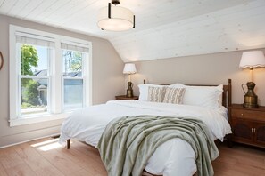 Een slaapkamer met een groot bed, twee bedlampen, een raam met zonwering en een schuine plafond.