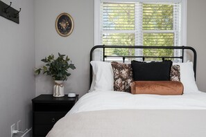 Een slaapkamer met een bed, een nachtkastje, een potplant, een fotolijst en een raam met jaloezieën.