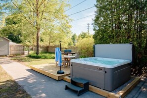 Een hottub met een houten terras, een tafel met stoelen en een barbecue in een achtertuin.