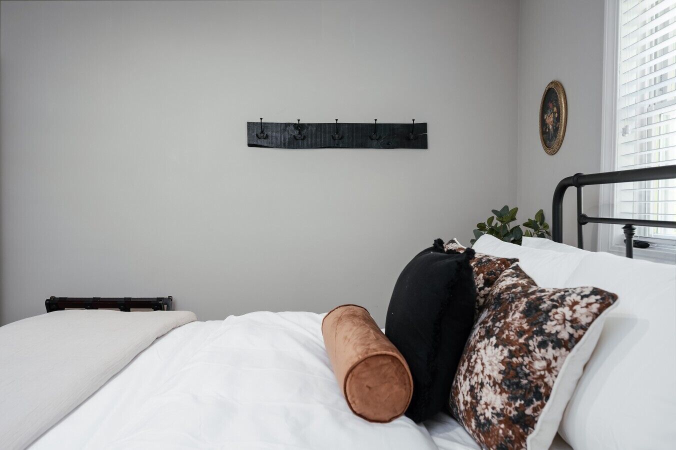 A bedroom with a bed, a headboard, a wall-mounted light fixture, and a window with blinds.