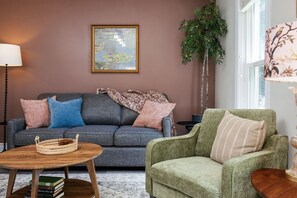 Un salon avec un canapé gris, un fauteuil vert, une table basse en bois, un tableau encadré au mur et une plante en pot.