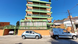 A multi-story hotel with balconies, a car parked in front, and a van with a logo. - El Mirador (Villa Carlos Paz)