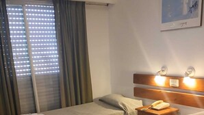 A hotel room with two beds, a bedside table with a phone, a window with curtains, and a wall-mounted light fixture. - El Mirador (Villa Carlos Paz)