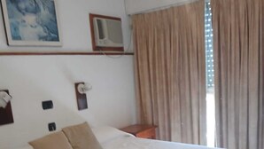 A hotel room with a bed, pillows, a nightstand, an air conditioning unit, a painting, and a window with curtains. - El Mirador (Villa Carlos Paz)