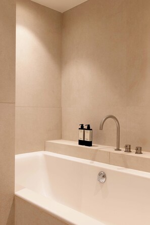 Ein modernes Badezimmer mit einer Badewanne, einem Wasserhahn und zwei Shampooflaschen auf einem Regal.