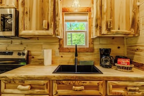 A kitchen with wooden cabinetry, a stainless steel microwave, a coffee maker, and a window with a view of trees. - 10 Minutes from downtown. Valley Hideaway Cottage (Sevierville)