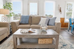 Ein Wohnzimmer mit einem beigefarbenen Sofa, einem Holztisch und Blick ins Freie durch große Fenster.
