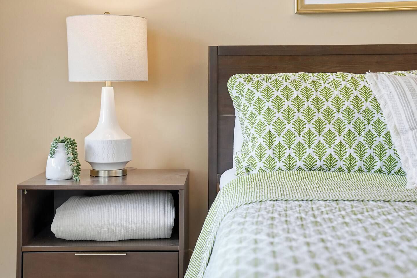 A neatly made bed with a patterned pillow and a bedside lamp on a wooden nightstand.