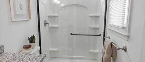 Un baño moderno con ducha envuelta en vidrio, inodoro, lavamanos con encimera de granito y toallero.