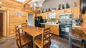 Una cucina in legno con tavolo da pranzo, sedie, frigorifero, fornello e microonde.