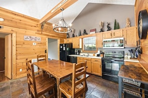 A wooden kitchen with a dining table, chairs, a refrigerator, stove, and a microwave. - Cedar Ridge Haven | Hot Tub, Fireplace & More! (Gatlinburg)