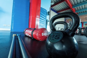 A kettlebell, red boxing gloves, and a barbell on a gym floor with blue walls and a brick wall in the background. - Hippie Nice Hostel (Mexico City)