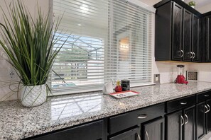 A kitchen with a granite countertop, black cabinets, a potted plant, a window with blinds, and a red appliance. - 4BR family retreat - 15 mins to Disney (Kissimmee)