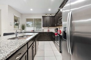 A modern kitchen with granite countertops, stainless steel appliances, and dark cabinetry. - 4BR family retreat - 15 mins to Disney (Kissimmee)