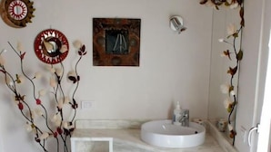 A bathroom with a white sink, a mirror, a decorative wall piece, and a floral rug. - CORTE BARBIERI (Ceraino)