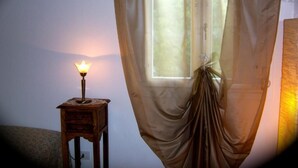 A room with a window covered by sheer curtains, a small table with a lamp, and a wall-mounted light fixture. - CORTE BARBIERI (Ceraino)