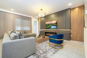 Ein modernes Wohnzimmer mit Sofa, einem blauen Sessel, einem Couchtisch, einem Flachbildfernseher und einem Kamin.