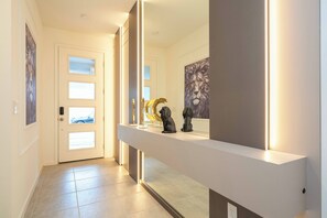 Ein moderner Flur mit einer weißen Tür, einer langen weißen Theke mit Dekoration und einem großen gerahmten Kunstwerk an der Wand.