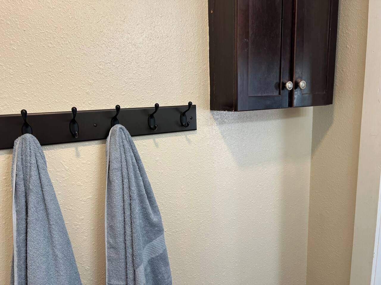 Une salle de bain avec un porte-serviettes sur lequel sont posées deux serviettes, un meuble en bois foncé et un mur à texture.