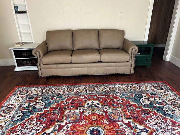 A beige sofa, a patterned rug, and a green cabinet in a room with wooden flooring.