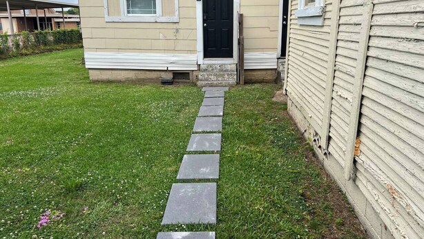 Una casa con puerta principal, un pequeño porche y un camino de piedra que lleva a la puerta.