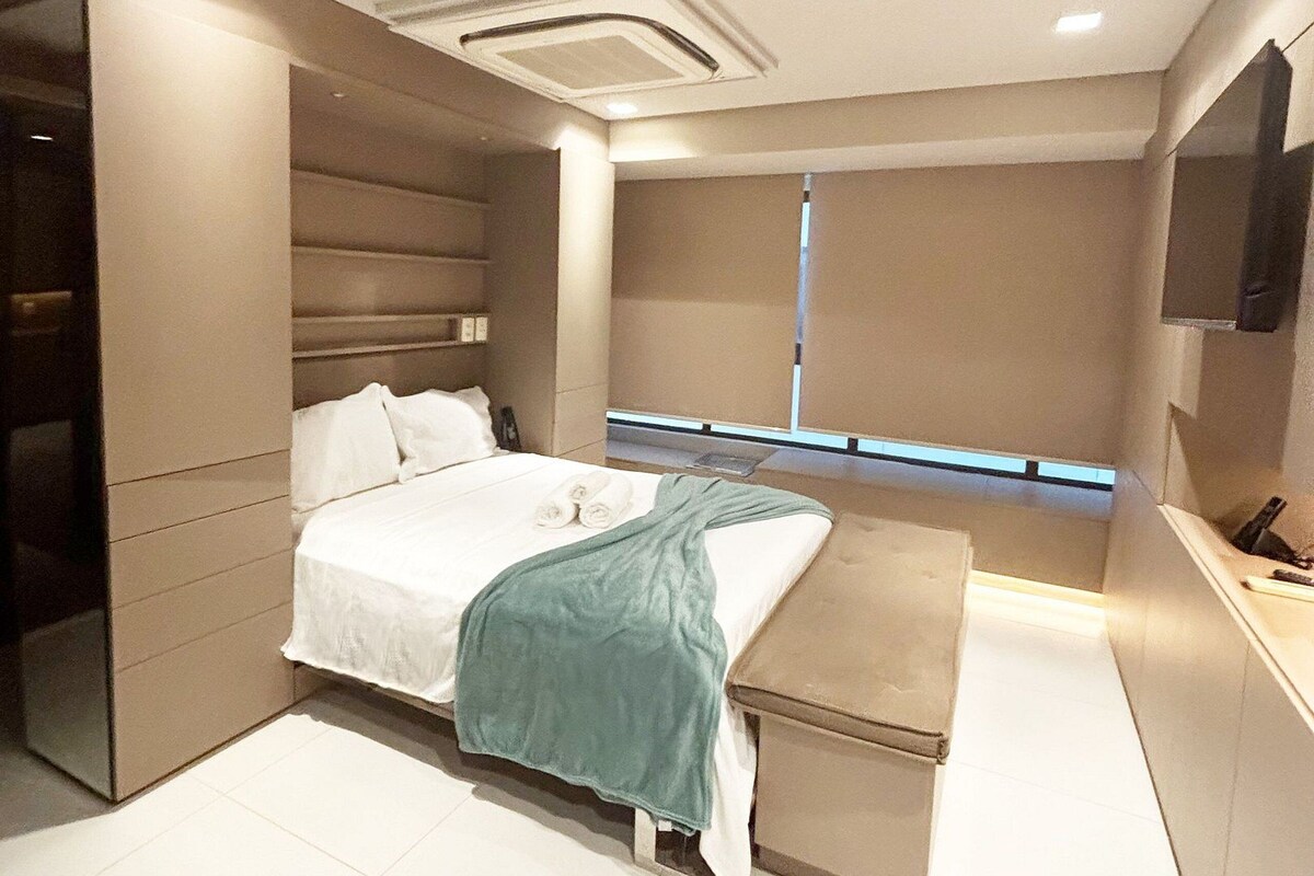 A modern bedroom with a bed, a bench, a TV, and a window.