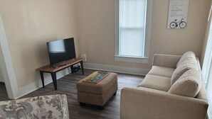 Ein Wohnzimmer mit einer Couch, Hocker, Fernseher und einer Wand mit einem Kunstwerk zum Thema Fahrrad.