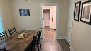 Ein Essbereich mit Holztisch und -stühlen, eine Küche im Hintergrund und ein gerahmter Spruch an der Wand.