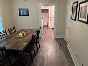 Un coin repas avec une table et des chaises en bois, une cuisine en arrière-plan et une citation encadrée accrochée au mur.
