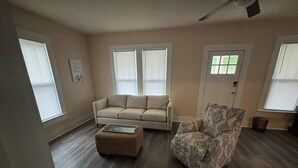 Ein Wohnzimmer mit einem beigen Sofa, einem gemusterten Sessel und einem Hocker.